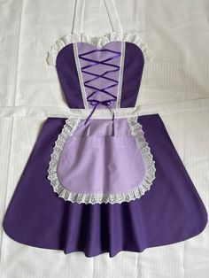 a purple apron with white lace around the waist and straps on it, sitting on a bed