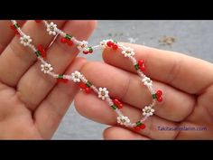 two hands are holding beads with red and white flowers on them in the shape of hearts