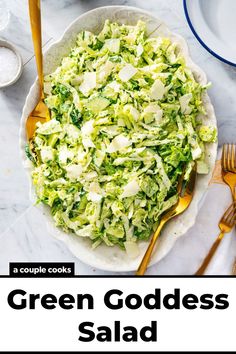 a white bowl filled with green goddess salad on top of a marble table next to gold utensils