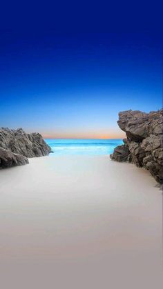 an empty beach with rocks and water in the background