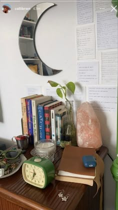 a wooden table topped with books and a green clock next to a mirror on the wall