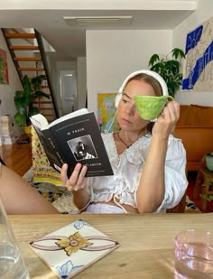 a woman sitting at a table with a book in front of her and holding a cup