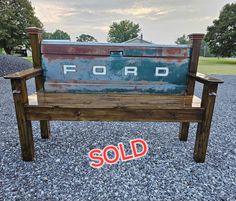 an old wooden bench sitting on gravel with a sold sign in front of it that says ford