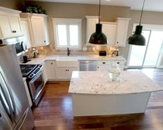 a kitchen with white cabinets and marble counter tops, stainless steel appliances and black pendant lights