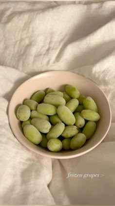 a white bowl filled with green beans sitting on top of a white bed cover covered in sheets