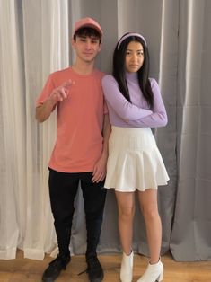 a man and woman standing next to each other in front of a curtain with their arms crossed