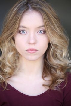 a woman with long blonde hair and blue eyes looking at the camera while wearing a red shirt