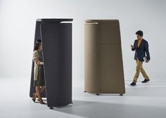 a man and woman walking past two tall speakers