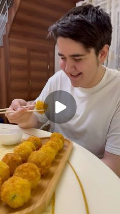 a man sitting at a table eating food with chopsticks in front of him