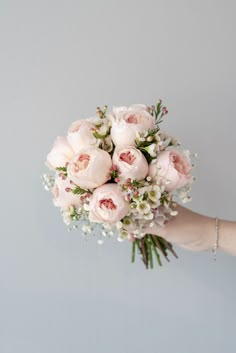 a person holding a bouquet of flowers in their hand on a gray background with white and pink flowers