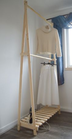 a white dress is hanging on a clothes rack next to a pair of shoes in front of a window