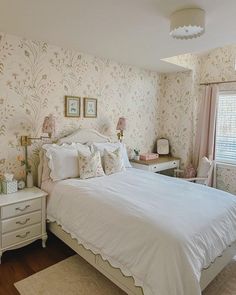 a white bed sitting in a bedroom next to a window with pink flowers on it