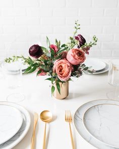 a table set with plates, silverware and flowers in a gold vase on top