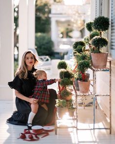 a woman holding a baby next to potted plants