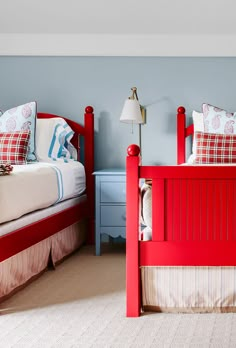 two red twin beds in a bedroom with blue walls and carpeted flooring, one is made from wood