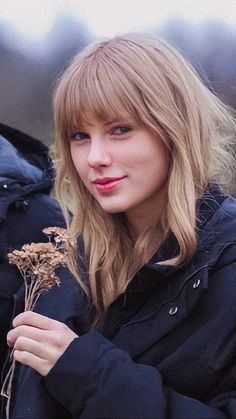 a woman with blonde hair is holding a dried plant in her hands and looking at the camera