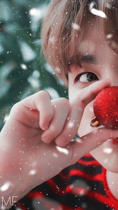 a young boy holding an apple in front of his face with snow falling around him