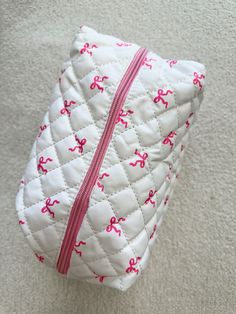 a white quilted bag with pink bows on the side and zippers down to it