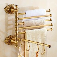 an antique brass towel rack with four towels hanging from it's sides and three hooks on the wall