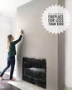 a woman is painting the wall in her living room with white paint and black fireplace mantel