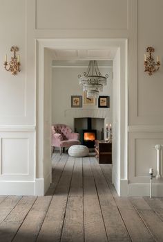 an open door leading to a living room with white walls and wood flooring, chandelier hanging from the ceiling