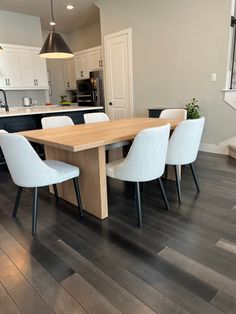 a dining room table with white chairs and an island in the middle is surrounded by wood flooring