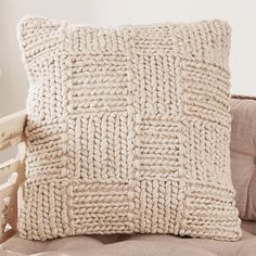 a white knitted pillow sitting on top of a couch next to a wooden chair