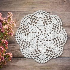 a white doily sitting on top of a wooden table next to pink and purple flowers