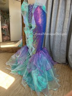 a mermaid costume sitting on top of a wooden floor in front of a curtained window