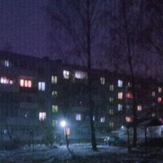 an apartment building lit up at night with street lights in the foreground and snow on the ground