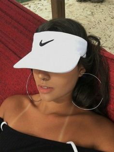 a woman wearing a nike visor while laying on a red couch with her hair in a ponytail