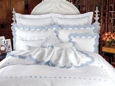 a bed with white sheets and blue trimmings is shown in front of a wooden headboard