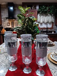 three clear glass vases sitting on top of a red table cloth in a kitchen