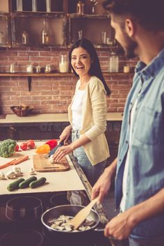 two people in the kitchen preparing food and smiling at each other while they are cooking