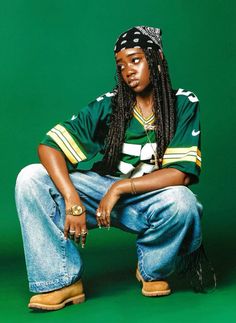 a man with dreadlocks sitting on the ground wearing jeans and a green shirt