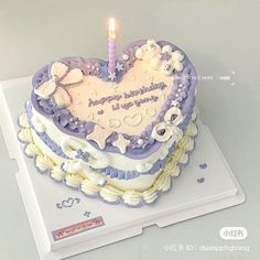 a heart shaped cake with a lit candle on the top is decorated in purple and white