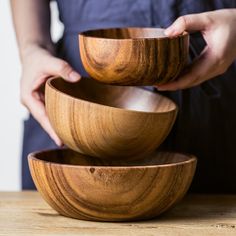 two wooden bowls stacked on top of each other in front of a person's hands