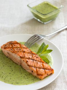 a white plate topped with salmon covered in green sauce and garnished with mint