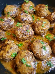 some meatballs are being cooked in a sauce with parsley on the top and green garnish