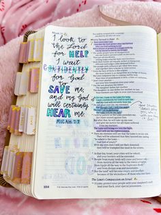 an open bible with handwritten words on the page and pink flowers in the background