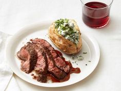 a piece of steak on a white plate next to a glass of red wine and bread