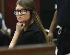 a woman with glasses sitting at a table in front of other people and looking off to the side