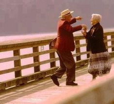 an older man and woman dancing on a pier