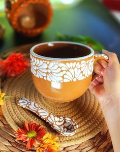 a hand holding a cup of coffee on top of a wicker tray with flowers