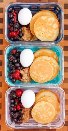 two plastic containers filled with pancakes, berries, and eggs on top of a wooden table