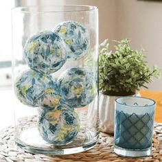 a glass vase filled with balls sitting on top of a table next to a potted plant