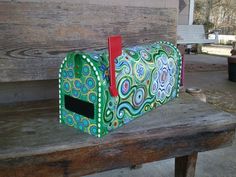 a green and red mailbox sitting on top of a wooden bench