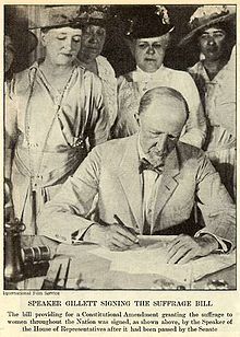 an old black and white photo of a man signing a document with other people in the background