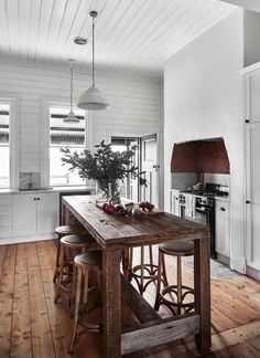 a kitchen with white walls and wooden floors, an island table surrounded by stools