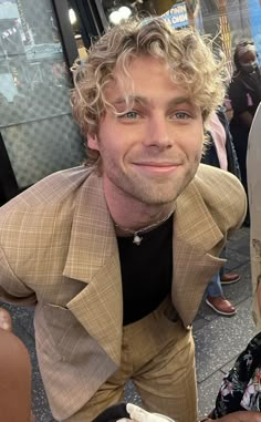 a man with curly hair is smiling at the camera while sitting on a bench in front of a crowd